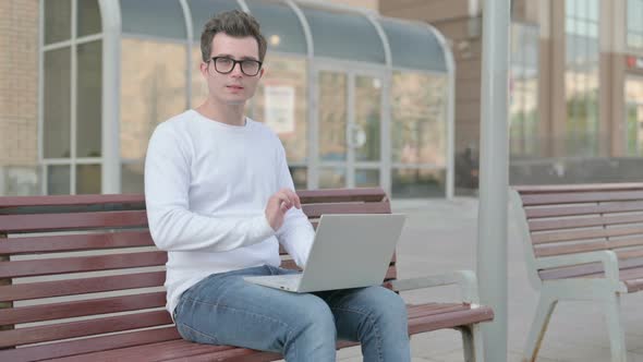 Young Man with Laptop Smiling at Camera While Sitting Outdoor on Bench