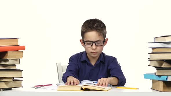 Boy Sits at the Table Leafing Through the Book. White Background