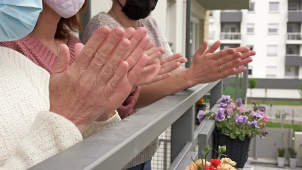 Three Women in Medical Masks, Standing on the Balcony of an Apartment Building, Cheerfully Applaud