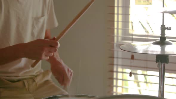 Drummer practicing slow drum beat rudiments on his home drum kit with natural light pouring through