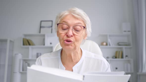 Emotional grey haired grandmother with glasses reads fairytale book