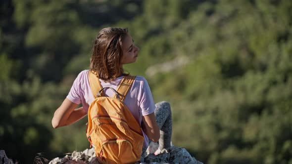 Rear View Girl Hiker Sits on Edge of High Cliff Enjoying Beautiful Seascape of Aegean Coastline