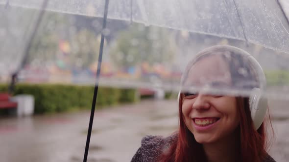 Young Beautiful Woman with Transparent Umbrella Dancing in Rain on City Street