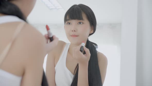 Beautiful young asian woman applying lipstick red on mouth, beauty girl looking facial at mirror.