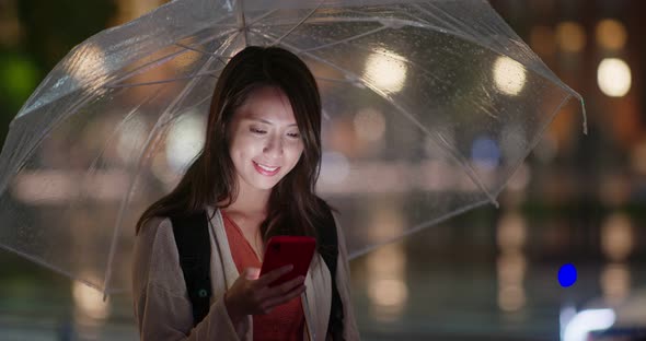 Woman hold with umbrella and use of mobile phone in the city at night