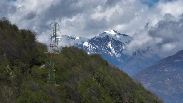 Power line towers on alp hilltop with scenic pointed mountain background view
