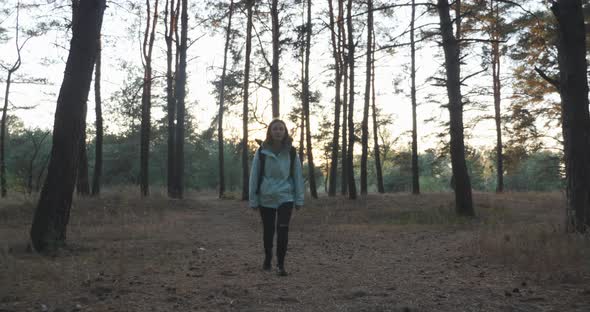 Young tourist traveler in blue jacket with tourist backpack hiking in fall forest at sunset