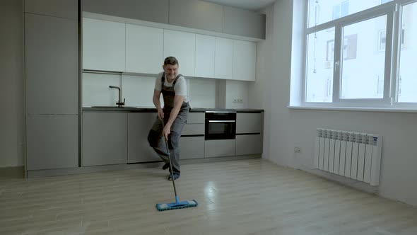 A Cheerful Worker in Uniform Washes the Floor in a New Apartment