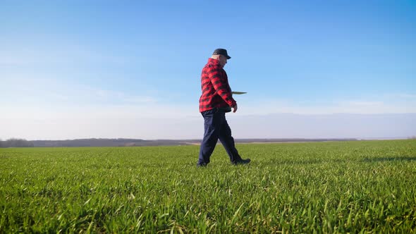 Senior Agronomist Man Looks at a Fresh Green Field After Winter. Smart Farming, Using Modern