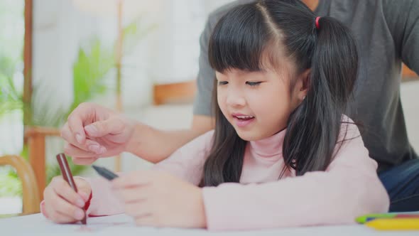 Asian young little kid daughter artist having fun drawing and coloring picture with father on table.