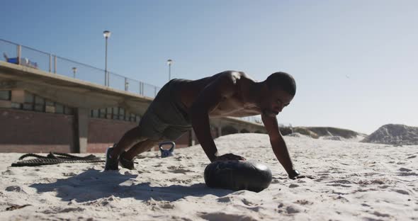 Focused african american man doing press ups on ball, exercising outdoors on beach
