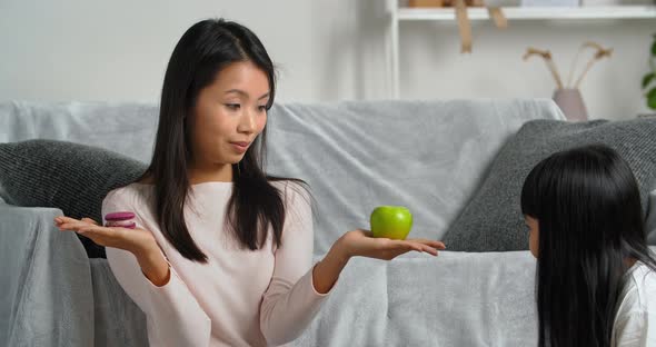 Asian Woman Single Mother Sitting at Home with Her Daughter Holding Cookies and Apple in Two Hands