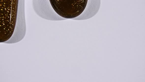 Brown Cosmetic Gel Fluid Gold Interspersed Flowing with Down on a White Surface