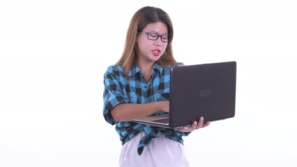 Happy Young Asian Hipster Woman Talking While Using Laptop