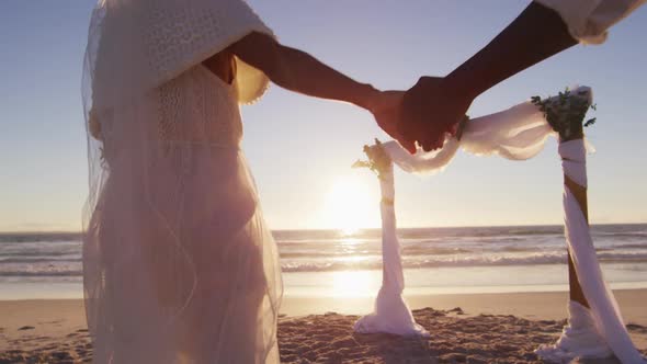 African american couple in love getting married, holding hands on the beach at sunset