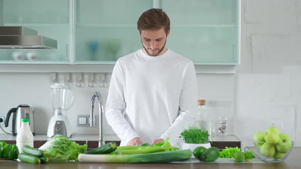 Man Prepares a Salad in the Kitchen Cuts Herbs and Green Vegetables to Make a Healthy Salad