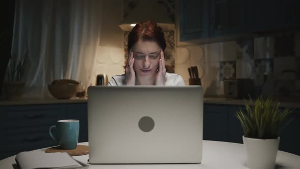 Woman In The Kitchen With Laptop. Woman Tired. Her Head Hurts