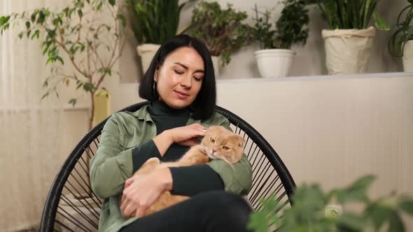 Woman sitting on the armchair holding cute ginger cat,