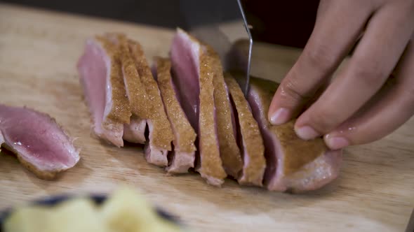 Cutting Pink in the Center Duck Breast into Slices on a wooden Chopping Board