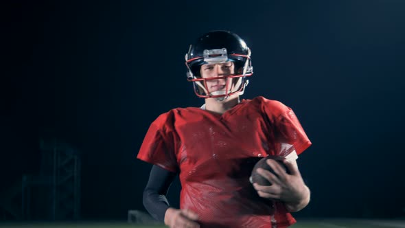 American Football Player Walks on a Field, Holding a Ball in Hands, Close Up.