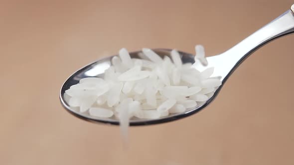 White long rice close up is poured into a metal spoon on the background of the board