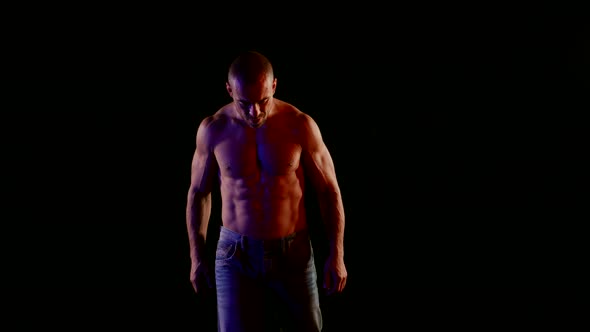 a Muscular Bald Man with a Bare Torso and Jeans Tilted Head and Walks Forward Then Raises Fists to