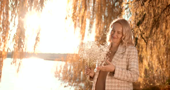 Pregnant Blonde Woman with a Bouquet on the Shore of the Pond