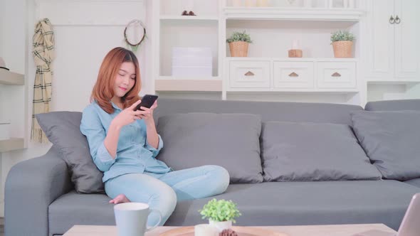 Asian woman using smartphone while lying on the sofa