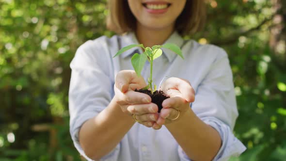 Asian woman holding plant in garden smiling on sunny day