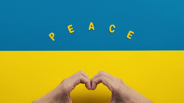 Hands Make Heart Symbol on Ukraine Flag with Peace Inscription