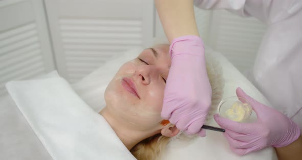 A Young Woman Gets A Procedure From A Beautician.Cosmetologist Making Cosmetic Facial White Mask 