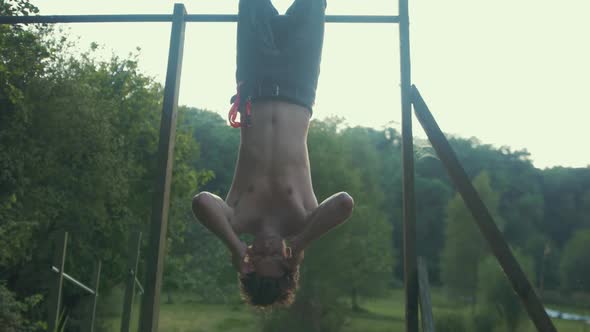 Young fit topless male doing sit up exercise for strengthening core upside down on pull ups bar outd