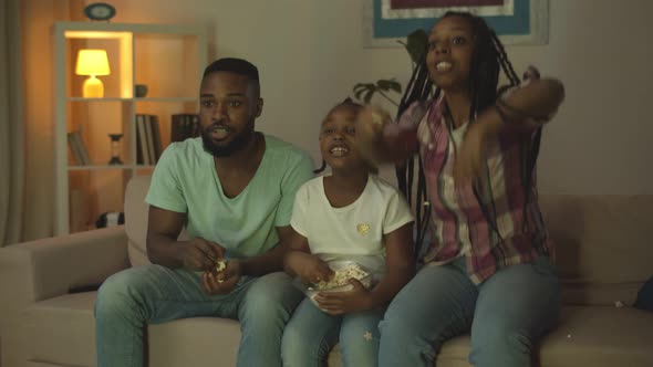 Afroamerican Mom Dad and Daughter Watching Sports Game on Tv and Eating Popcorn