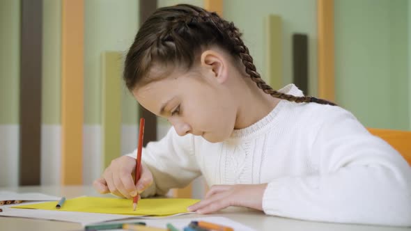 Closeup Side View of Pretty Concentrated Girl Painting with Pencil Sitting at Desk