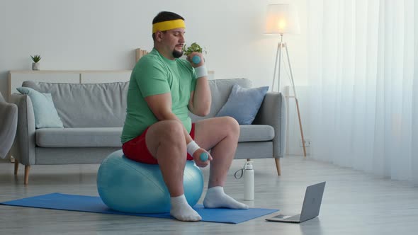 Overweight Guy in Sport Clothes Exercising with Dumbbells Sitting on Fit Ball and Watching Video