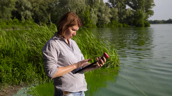 Adult Woman Ecologist Examines Sample of Green Algae and Enters Data on Tablet