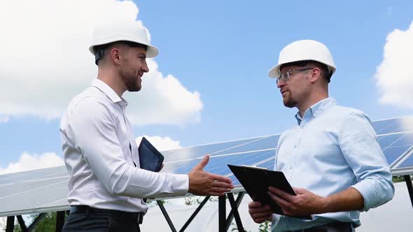 Two Male Engineer Wearing Safety Vest Handshake with Solar Panels Background