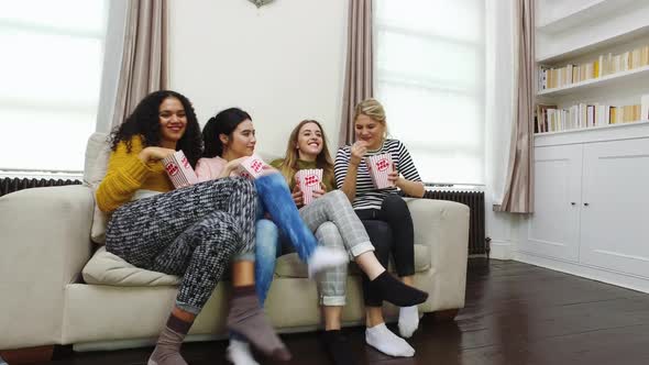 Female friends jumping on sofa and eating popcorn