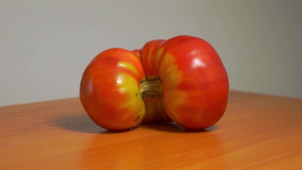 Big funny, twisted, curved, semi-circular, interesting, the tomato rotates on a wooden surface.
