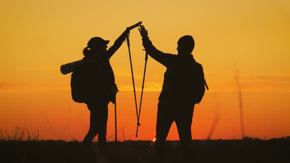 Silhouettes of Two Hikers with Backpacks Enjoying Sunset View From Top of a Mountain. Enjoying the