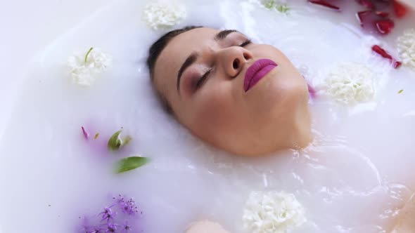 Closeup View of Young Woman's Face Bathing in Milk Bath Filled with Flowers and Getting Up