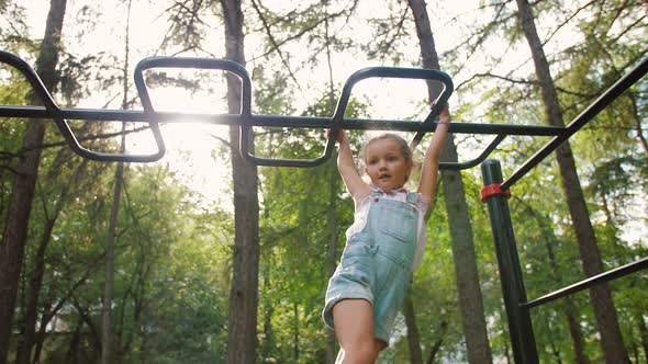 Little Girl Hanging and Climbing on Monkey Bars in Park on Workout Playground