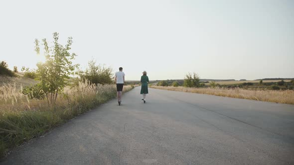 Back View of Couple Riding on Electric Scooters on Road on Nature at Sunset