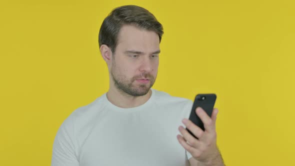 Young Man Loss on Smartphone on Yellow Background