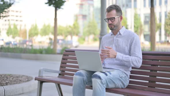 Young Adult Man Talking on Video Call While Sitting Outdoor on Bench