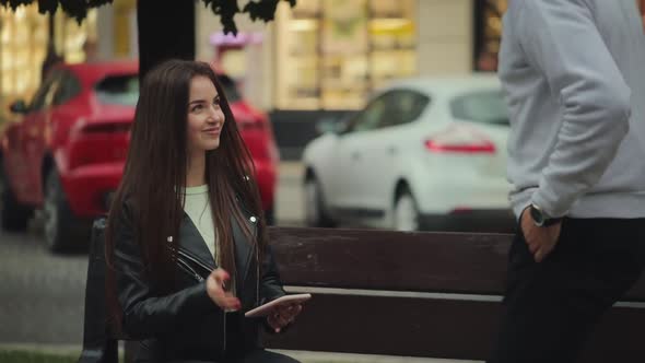 A Young Woman is Sitting on a Bench and Texting on Her Smartphone