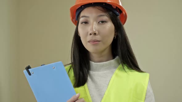 Young Female Builder in a Signal Vest and Helmet Writes Something