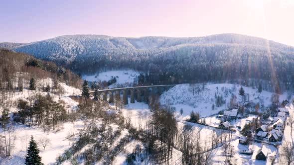 Winter mountain countryside with a railway viaduct in falling snow.
