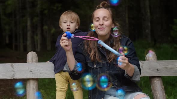 Positive Young woman with her sons playing with soap bubbles and enjoying vacation in the park.