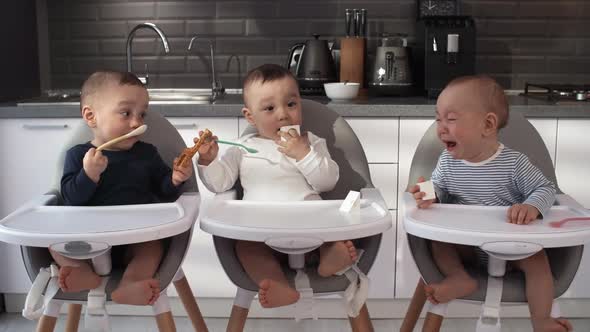 Asian Triplets Sitting in High Chairs in Kitchen and One Baby Crying